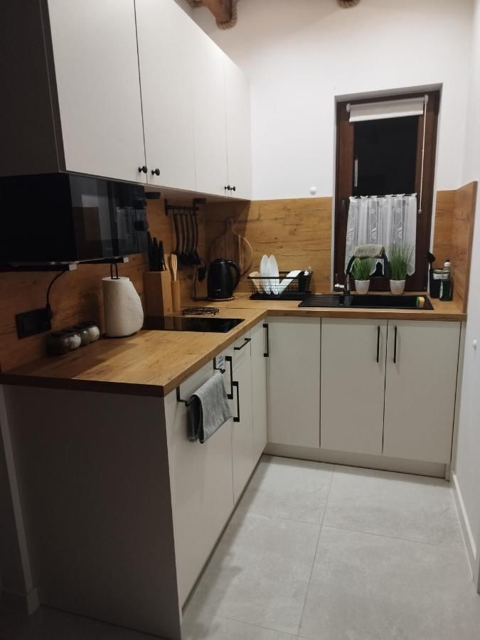 Kuchnia z białymi szafkami, drewnianym blatem, płytą i mikrofalówką