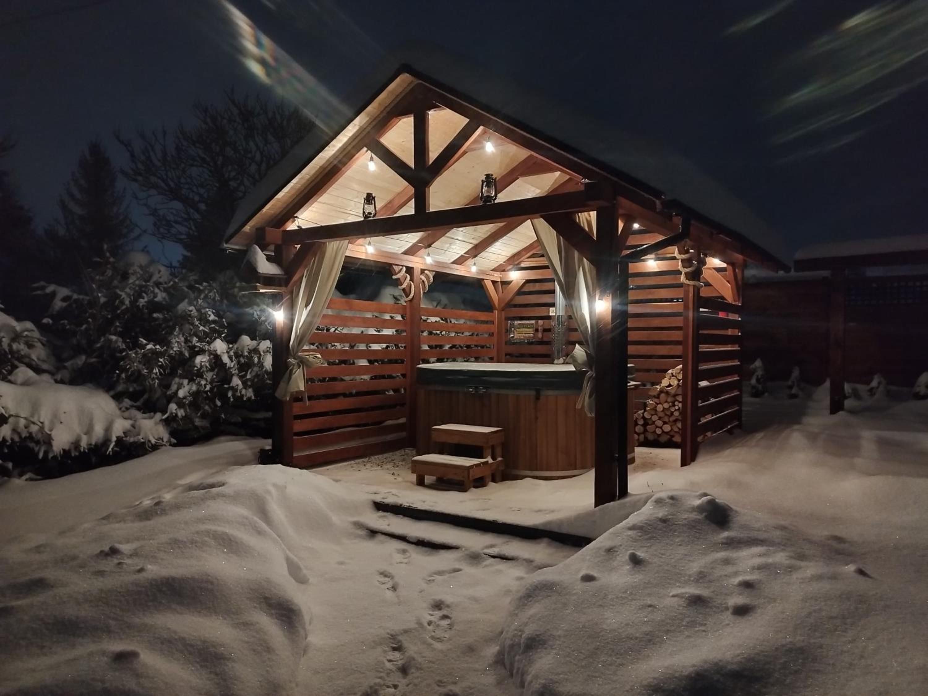 Oświetlona altana z jacuzzi nocą, dookoła śnieg