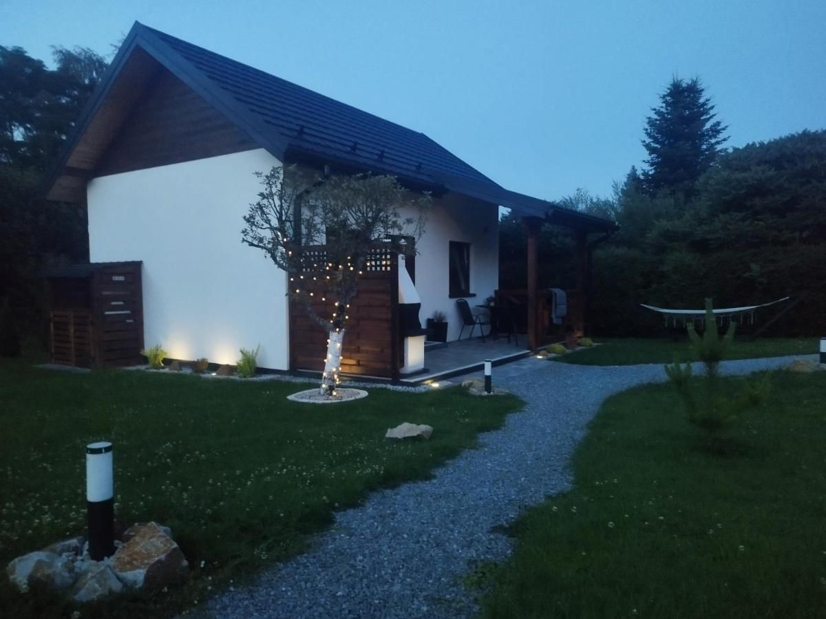 Dom o zmroku, drzewko przy tarasie świeci lampkami, ogród oświetlają słupki